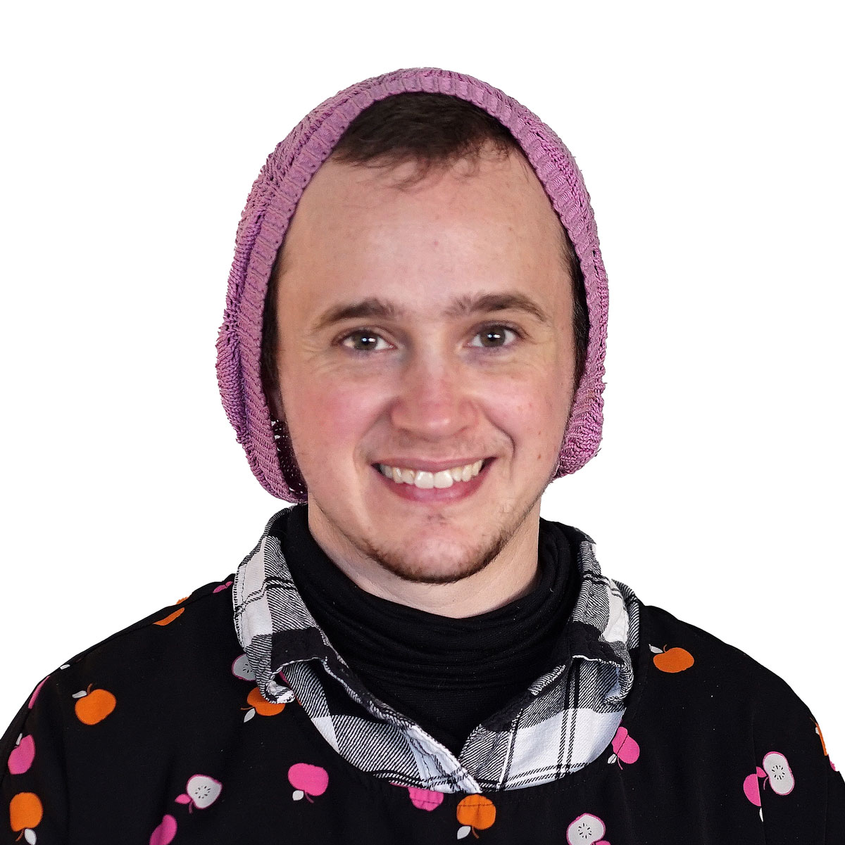 Leo, smiling wearing a pink slouchy beanie and colorful tunic over a button up plaid shirt.